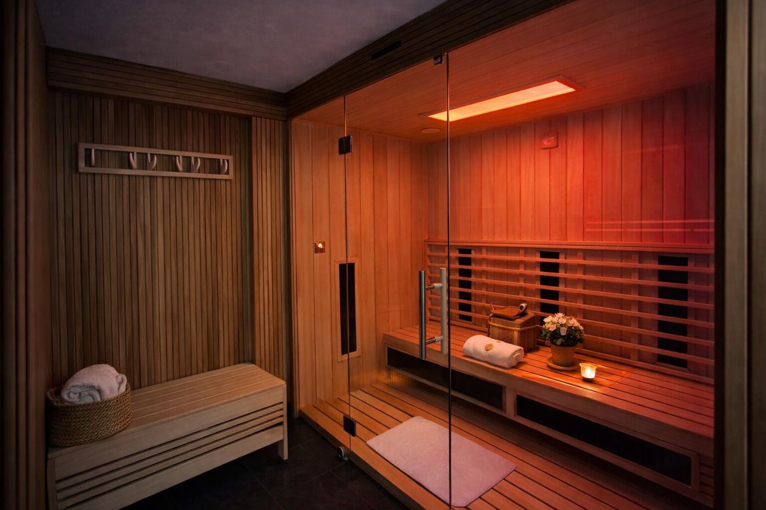 Una sauna con pareti in legno, una panca, un asciugamano, un tavolino con una candela e una pianta in vaso.