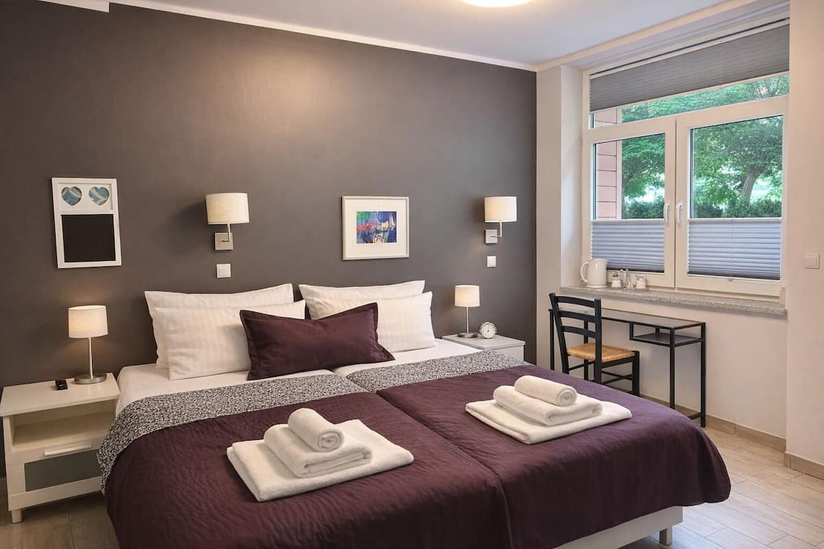 Una habitación de hotel moderna con una cama grande, dos mesitas de noche, un escritorio y una ventana con vistas a árboles.