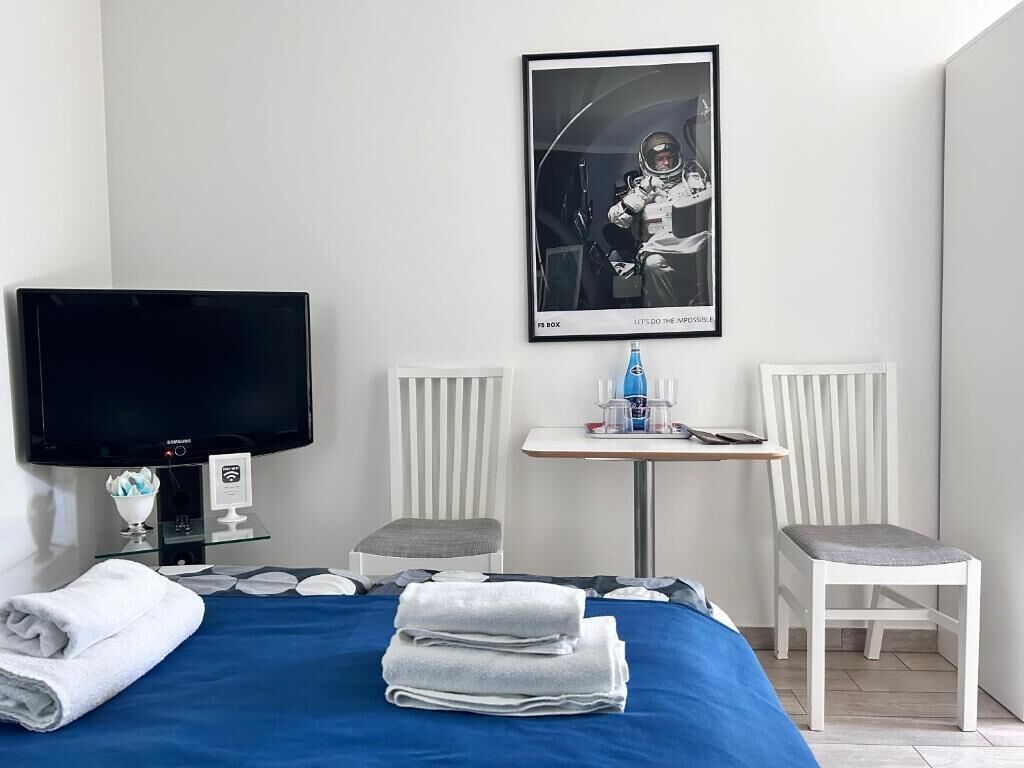 Een hotelkamer met een bed, een televisie, een kleintje tafeltje met een fles, twee stoelen, en een ingelijst kunstwerk aan de muur.