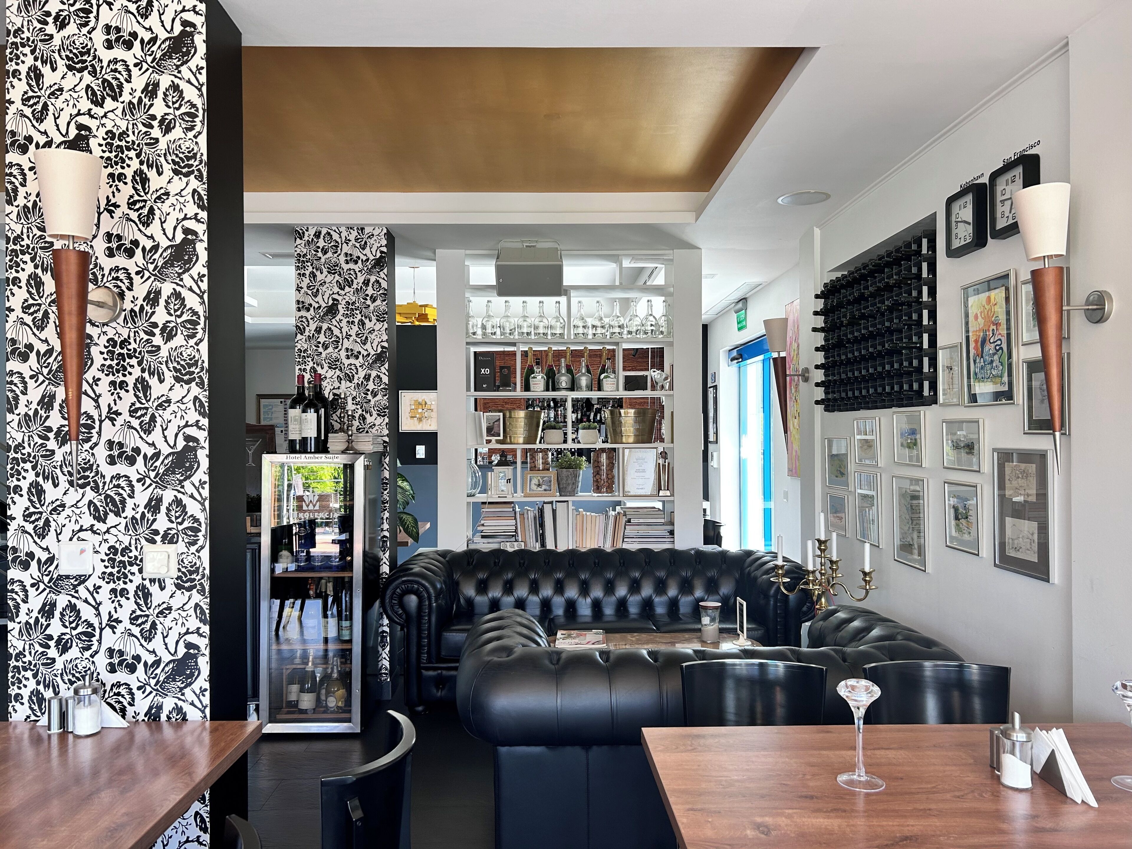 Una zona de bar moderna con un sofá de cuero negro, una estantería para vinos y obras de arte enmarcadas en las paredes.