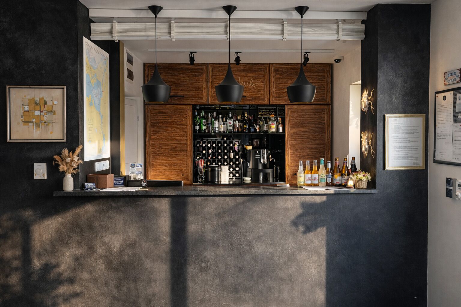 Un coin bar avec un buffet en bois rempli de bouteilles, des luminaires suspendus et une carte accrochée au mur.