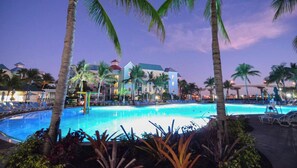 A resort pool area with palm trees, lounge chairs, and a building with multiple stories in the background. - 1 Bedroom Premium - Harborside Resort at Atlantis - Full Resort Access (Paradise Island)