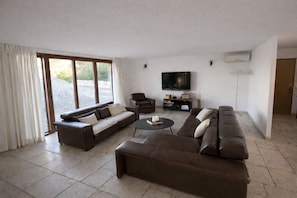 A modern living room with a large sectional sofa, a coffee table, and a flat-screen TV mounted on the wall.