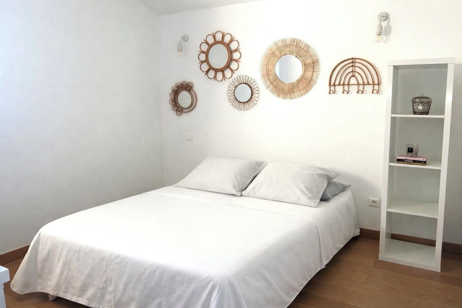 Een slaapkamer met een wit bed, twee kussens, een witte kledingkast en decoratieve spiegelwand.