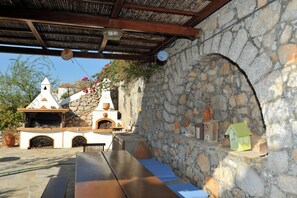 An outdoor patio with stone walls, a wooden pergola, and a rustic outdoor kitchen. - VILLA FIVOS (Hydra)