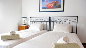 Een tweepersoonsbed met witte lakens en twee opgerolde handdoeken, een nachtkastje met een lamp, en een lijst met een foto aan de muur.