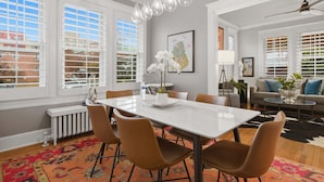 A modern dining area with a white table, brown chairs, and hanging pendant lights. - Charming 4BR Bungalow - Steps to Clarendon METRO (Arlington)