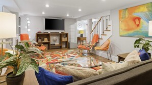 A modern living room with a flat-screen TV, a colorful rug, and a staircase. - Charming 4BR Bungalow - Steps to Clarendon METRO (Arlington)