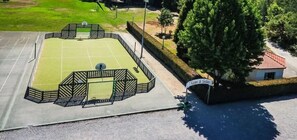 Una cancha de baloncesto al aire libre con una valla, un edificio pequeño y un cartel.
