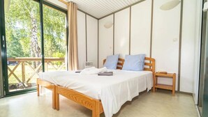 A bedroom with a wooden bed, white bedding, a nightstand, and a view of greenery outside.