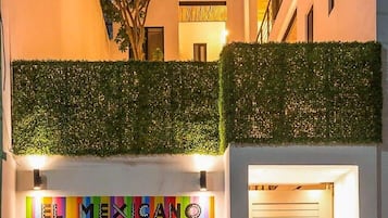 Fachada de edificio con un mural colorido que dice 'EL MEXICO' y una puerta de madera con persiana cerrada.