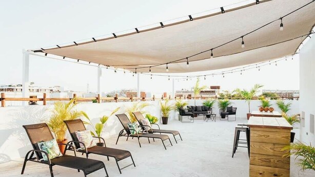 Une terrasse sur le toit, avec des chaises longues, une table en bois et des guirlandes lumineuses.