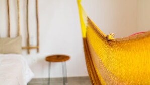 Un hamac dans une pièce où se trouvent un lit et un petit tabouret.