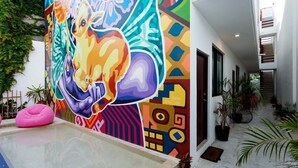 Een levendige muurschildering met abstracte patronen en een zwembadgedeelte met een roze loungestoel.