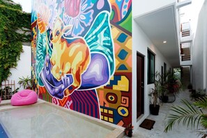 A vibrant mural with abstract patterns and a pool area with a pink bean bag. - King Studio Walk to Beach + Rooftop Pool (Playa del Carmen)