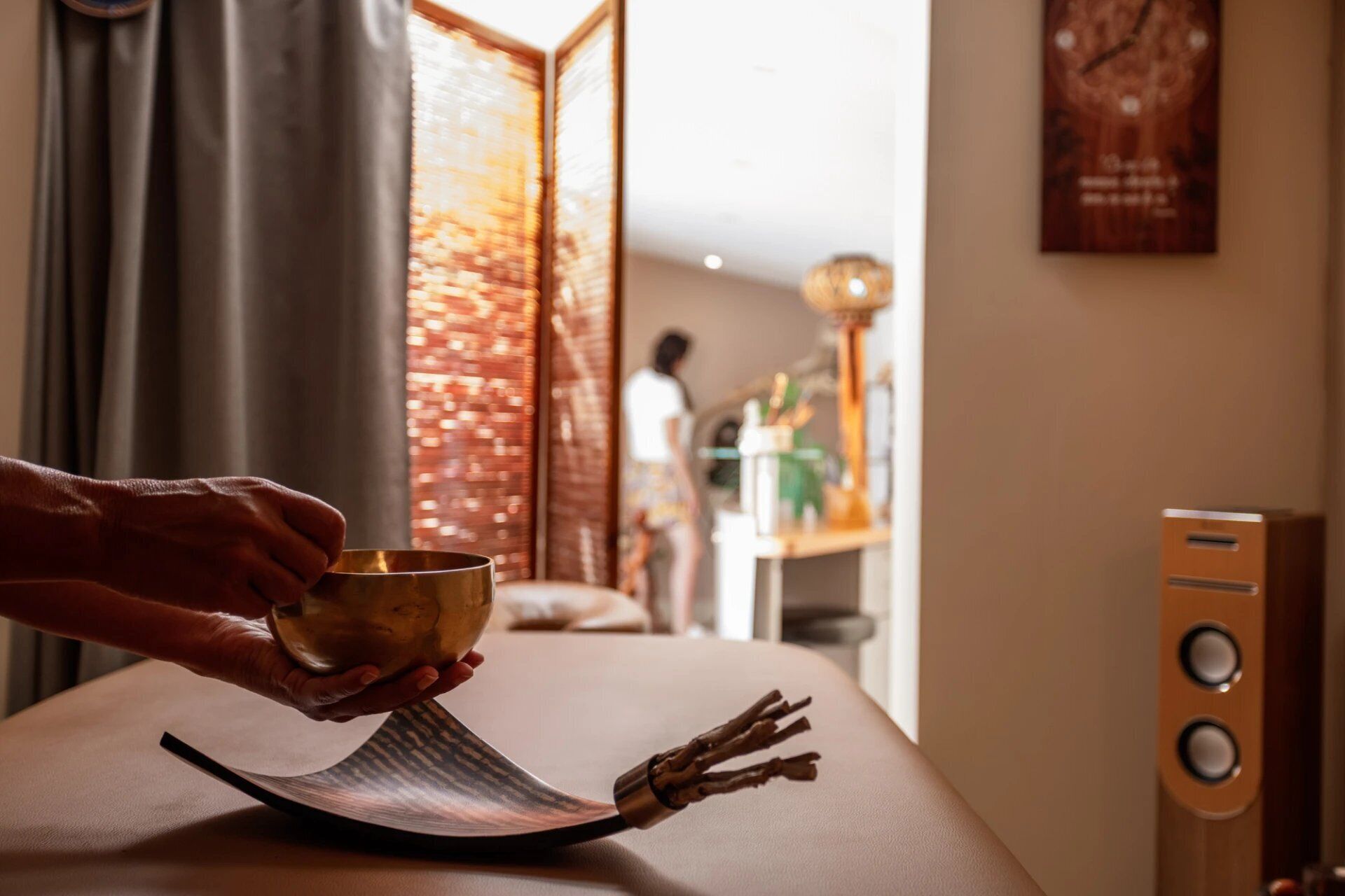 A hand holding a bowl over a table with a unique, curved table runner. In the background, a person is visible near a window with a view of a brick wall.