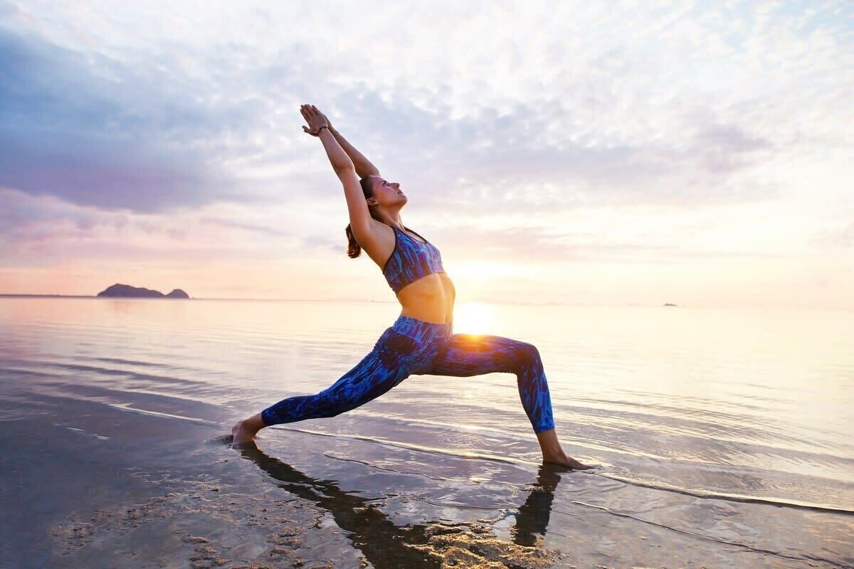 Une personne effectuant une posture de yoga sur une plage au coucher du soleil.