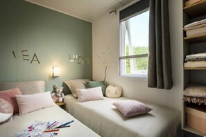 Een slaapkamer met twee bedden, een nachtkastje, een teddybeer en een muur waarop de tekst 'LEA' staat.