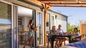 Un'area esterna coperta con tavolo e sedie, una porta scorrevole in vetro che dà su una cucina e una struttura in legno a pergola.