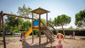 Un'area giochi con una struttura in legno per arrampicarsi, uno scivolo e altalene.