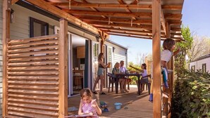 A wooden deck with a covered area, a dining table, and people sitting and standing. - ZEcamping 4* - espace aquatique de 2000m2 - proche cap d'Agde (Bessan)