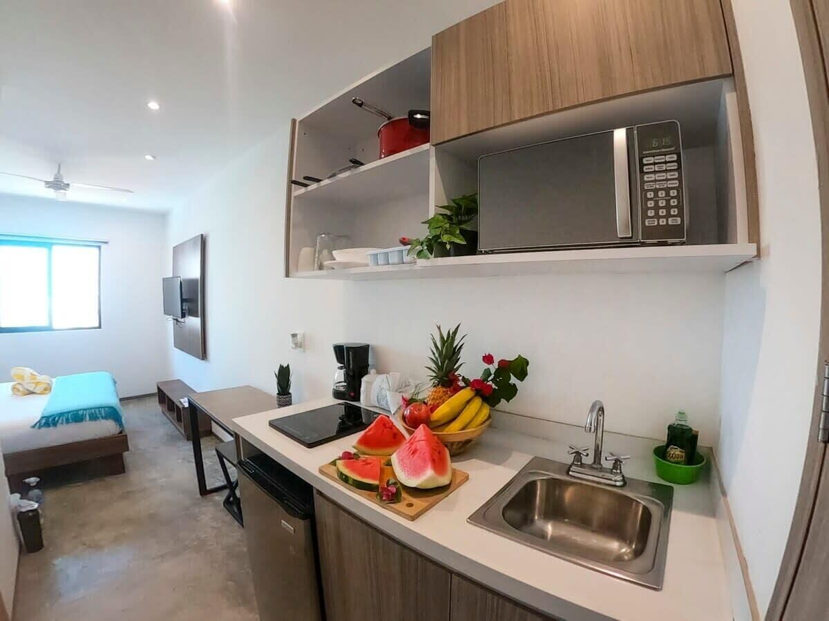 A compact kitchen with a microwave, sink, and a fruit bowl on the counter.