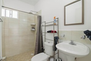 Et badeværelse med bruser, toilet og håndvask. Der er en bøjle med toiletartikler og et spejl over vasken.