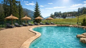 A swimming pool with lounge chairs and thatched umbrellas, surrounded by a grassy area and mountains in the background. - ZEcamping 3* toboggans dog friendly locatif 36m2 5 pers (Chézery-Forens)