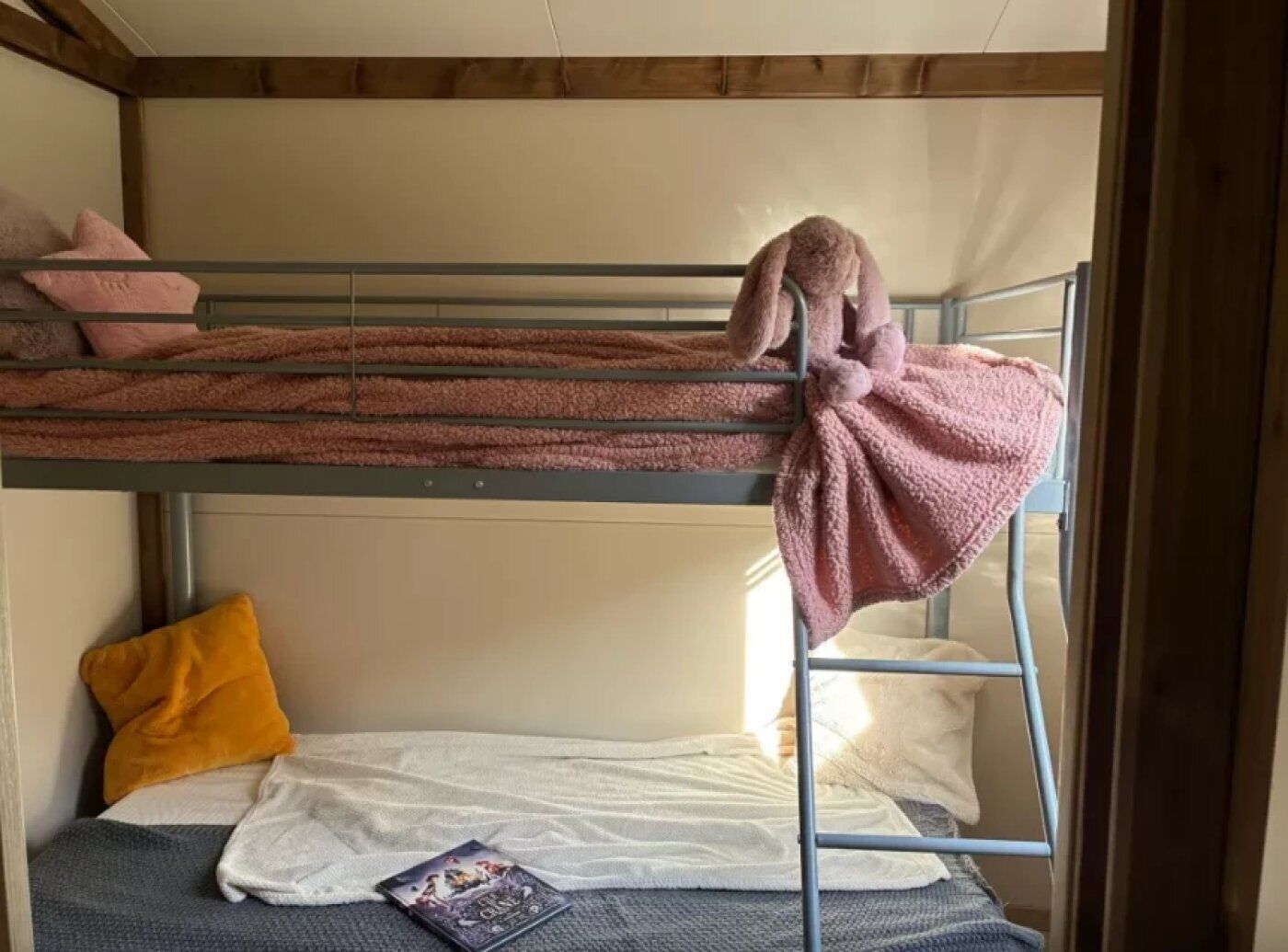 A bunk bed with a pink blanket and a stuffed toy on the top bunk.
