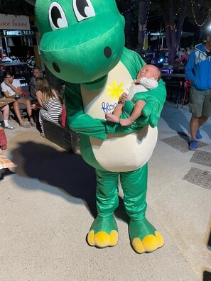 Eine Person in einem grünen Dinosaurierkostüm hält ein Baby.