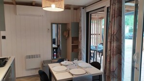A dining area with a table set for four, a ceiling light, and a view through a glass door to an outdoor seating area. - ZEcamping 3* parc aquatique locatif TV LV clim 70m2 (Saint-Maime)