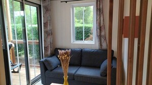 A room with a grey sofa, a yellow vase with dried flowers, and a window with a view of greenery. - ZEcamping 3* parc aquatique locatif TV LV clim 70m2 (Saint-Maime)