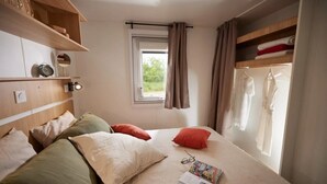 Et soveværelse med seng, puder, et natbord med lampe, et vindue med gardiner og en garderobe med tøj.