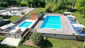 Ein Dachpool mit zwei Bereichen, umgeben von Holzterrasse und einer Rasenfläche mit Bäumen.