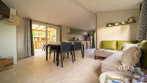 Un salon moderne avec un canapé, une table à manger et des chaises. On aperçoit un coin cuisine au fond.