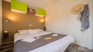 A neatly made bed with a gray blanket, a white pillow, and a magazine on it. There are two wall-mounted lamps on either side of the bed. - ZEcamping 4 étoiles animé piscine couverte locatif TV BBQ clim 32m2 (Laroque-des-Albères)