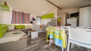 A compact living space with a green sofa, a dining table, and a kitchen area. - ZEcamping 4 étoiles animé piscine couverte locatif TV BBQ clim 32m2 (Laroque-des-Albères)
