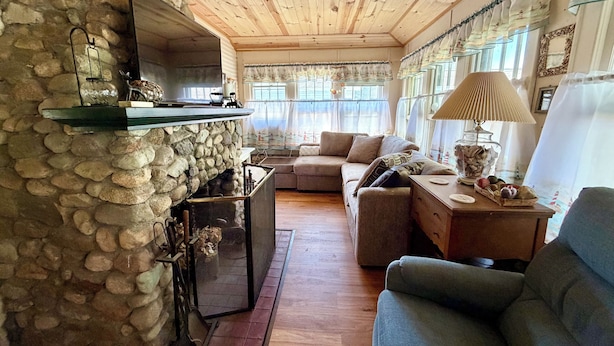 Una sala de estar acogedora con chimenea de piedra, techo de madera y ventanas amplias.