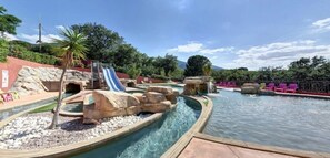 Un parque acuático con tobogán, formaciones rocosas y una zona de piscina.