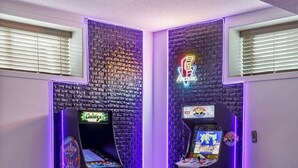 A room with a dark blue sofa, arcade games, and a neon sign. - Arcade, Neon Lights, 70 min Banff , Local Coffee (Calgary)