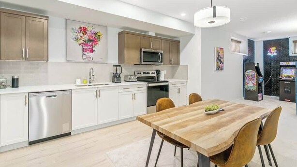 A modern kitchen with white cabinetry, a wooden dining table, and a black refrigerator. - Arcade, Neon Lights, 70 min Banff , Local Coffee (Calgary)