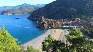 Un pueblo costero con una playa, afloramientos rocosos y terreno montañoso al fondo.