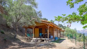 Una cabaña de madera con un porche, mobiliario exterior y un camino de tierra que la conduce.