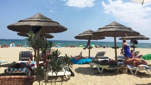Una playa con sombrillas de paja, sillas de descanso y una vista despejada del océano.