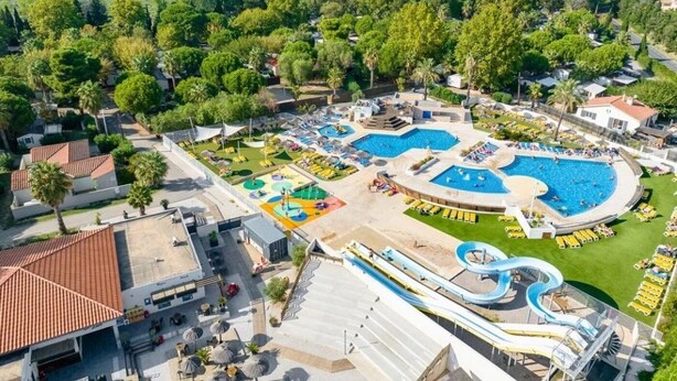 Vista aérea de un complejo turístico con varias piscinas, un tobogán acuático y diversas zonas de estar al aire libre.