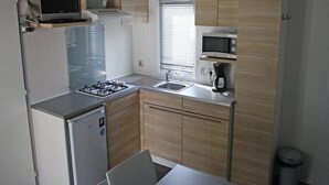 Una cocina compacta con estufa a gas, microondas, pileta y un refrigerador pequeño.