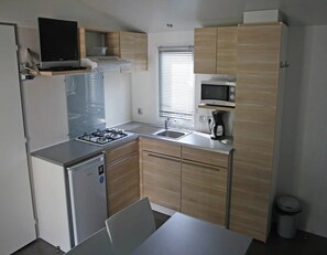 A compact kitchen with a gas stove, microwave, sink, and a small refrigerator. - ZEcamping 4 étoiles 3km plage parc aquatique mobil-home clim 29m2 (Saint-Cyprien)