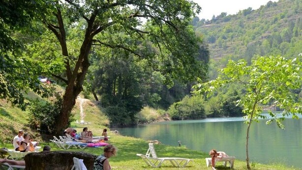 A lakeside setting with people relaxing on lawn chairs and a small tree. - ZEcamping 4* familial piscine pet friendly chalet TV BBQ clim 45m2 (Saint-Rome-de-Tarn)