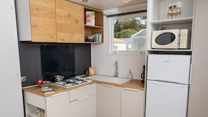 Cocina compacta con estufa a gas, armarios blancos, microondas y refrigerador.