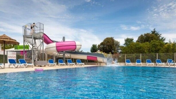 Una piscina con tobogán de agua, sillas de descanso y una torre de salvavidas.